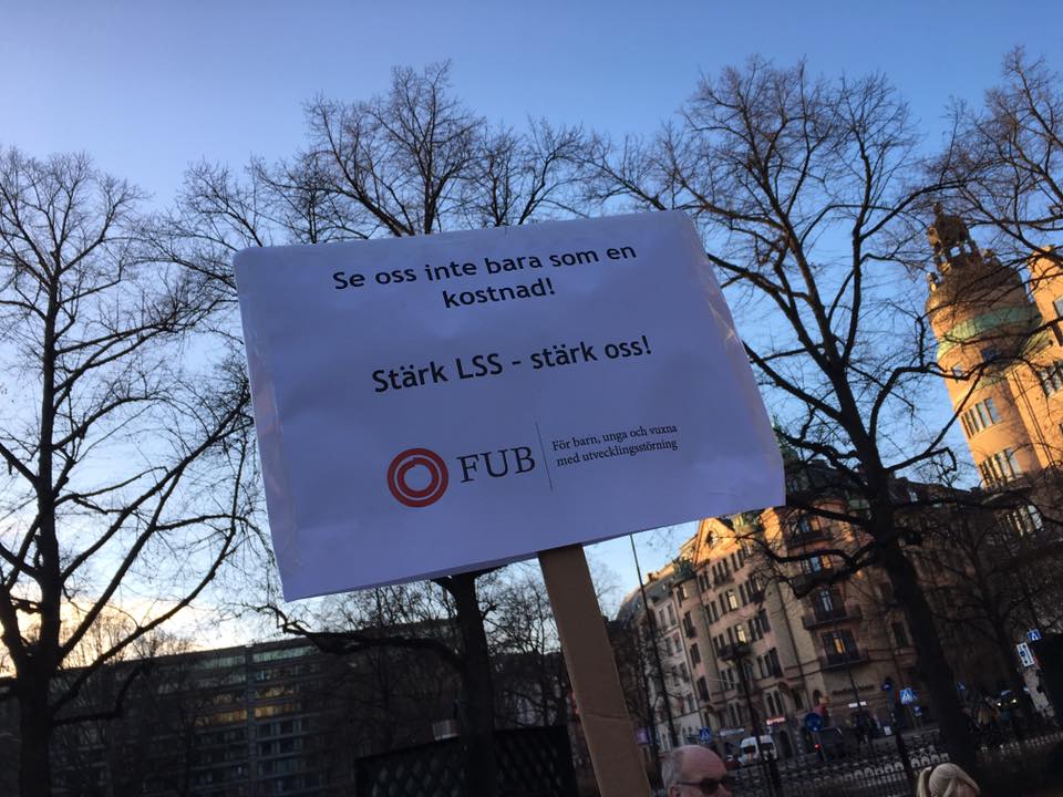 Skylt med texten &amp;quot;Se oss inte bara som en kostnad. Stärk LSS, stärk oss&amp;quot; på manifestationen &amp;quot;Assistans är frihet! Rädda LSS!&amp;quot; i Stockholm den 3 december 2016