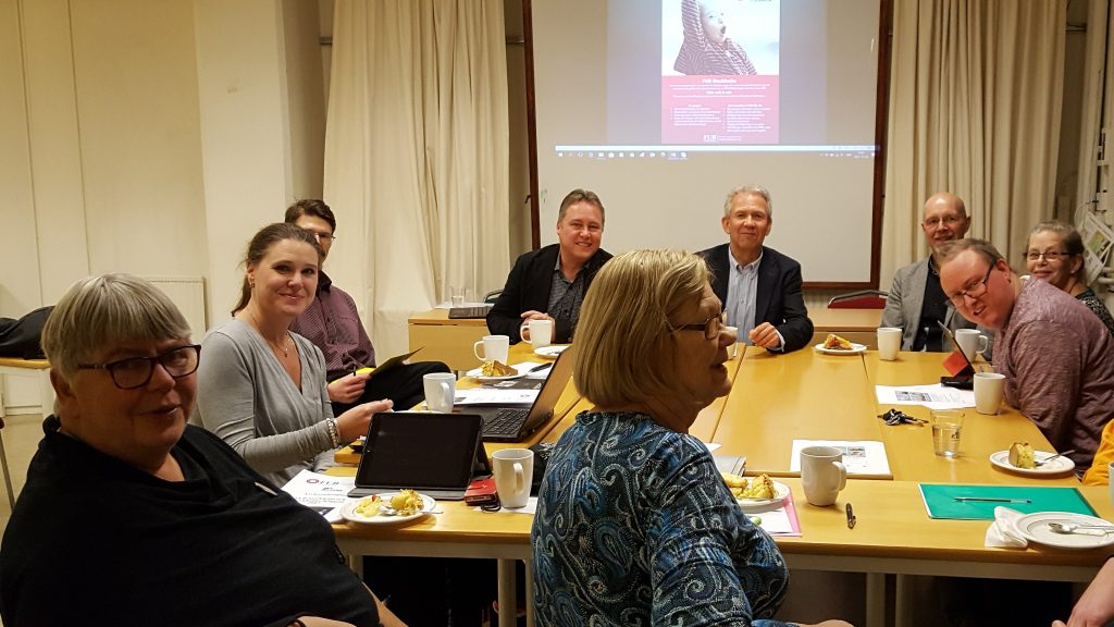 personer som sitter i möte, några ler mot kameran