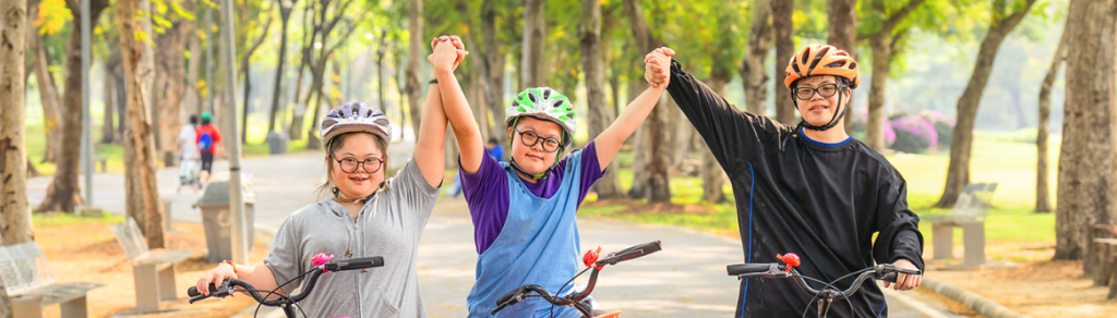 Tre ungdomar med cyklar som håler varandra i händerna och sträcker upp dem.